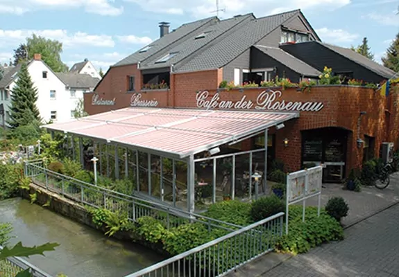 Grüne Terrassenmarkise für stilvollen Sonnenschutz Die T500 schützt eine Terrasse mit Glaselementen